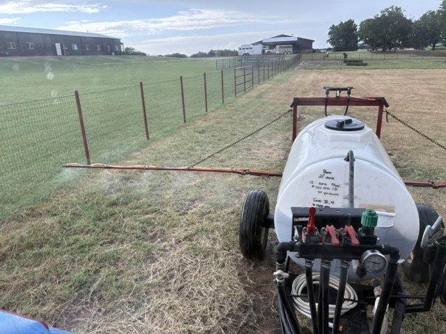 Pull-type sprayer with rates and field notes written on the tank, making a liquid fertility pass